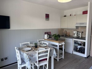 Une cuisine compacte avec des meubles blancs, une table à manger dressée avec des assiettes et des verres, et une machine à café.