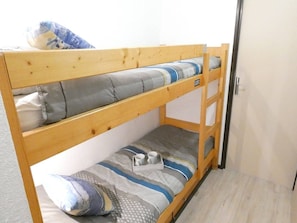Una cama individual con estructura de madera, ropa de cama gris y azul, y una mesita con una taza y una caja de pañuelos.