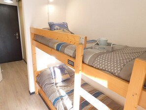 Un lit superposé avec une structure en bois, une petite table avec une tasse et un livre, et un oreiller orné d’un personnage de dessin animé.