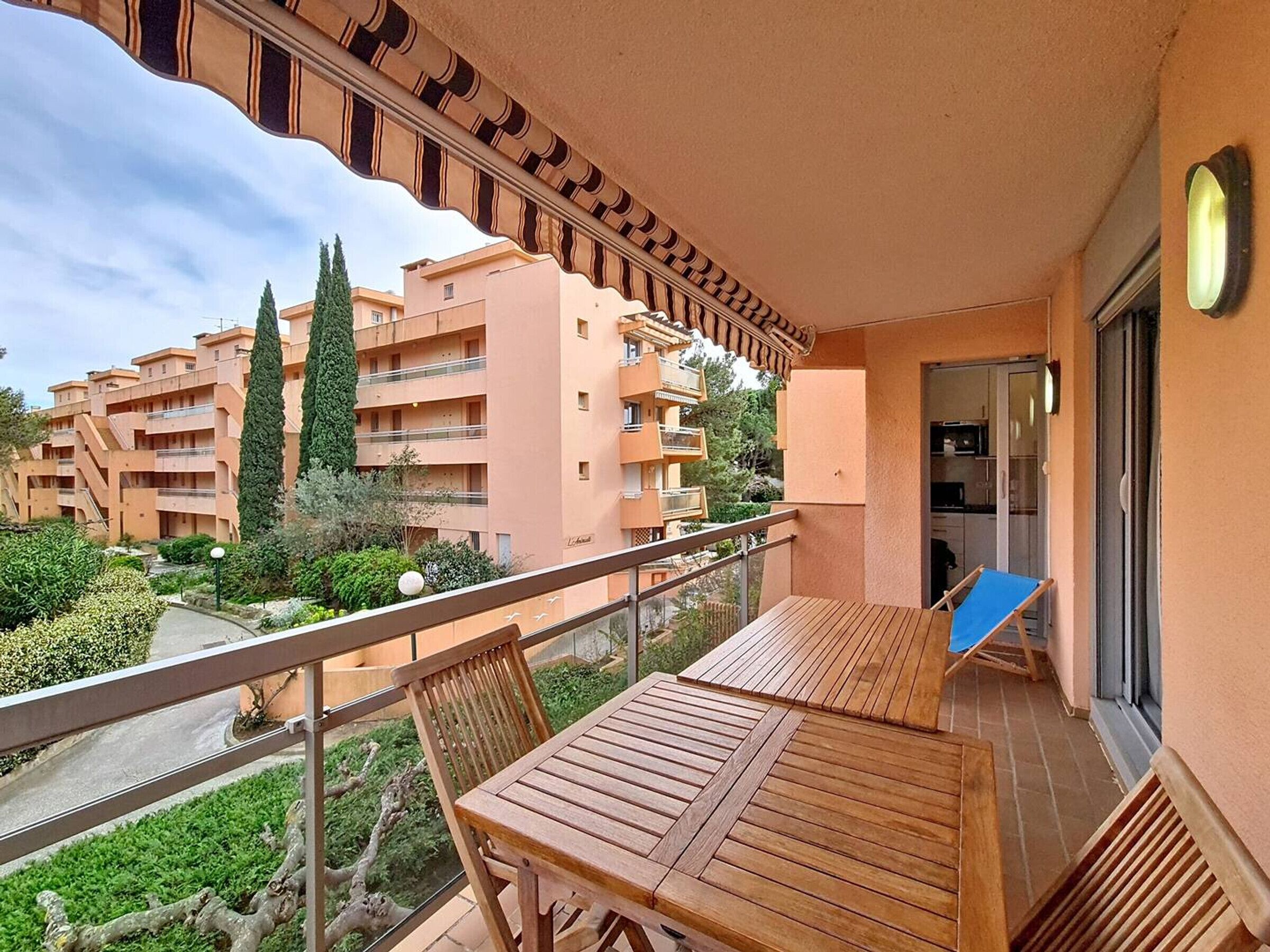 A balcony with a wooden table and chairs, overlooking a residential area with apartment buildings and greenery.