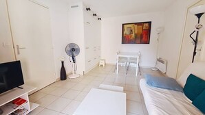 A modern living room with a TV, white furniture, a fan, and a painting on the wall.
