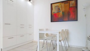 A modern kitchen with white cabinets, a dining table with chairs, and a large abstract painting on the wall.