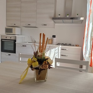 Una cocina moderna con armarios blancos, microondas, horno y estufa a gas. Hay un florero con flores sobre la mesa de comedor.
