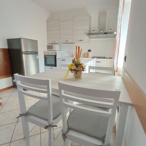 Una cocina moderna con armarios blancos, un refrigerador de acero inoxidable, un microondas y una estufa a gas. Hay una mesa de comedor con dos sillas y un florero con flores.
