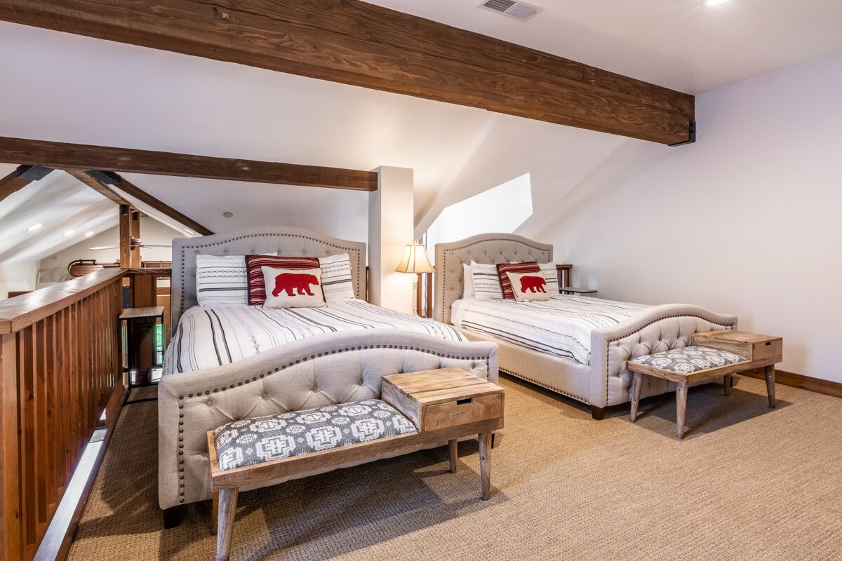 A bedroom with two beds, a wooden bench, and a sloped ceiling.