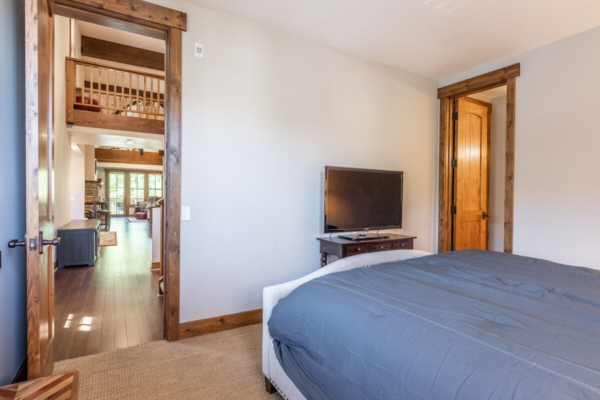 A bedroom with a large bed, a television on a wooden stand, and a wooden door leading to another room.