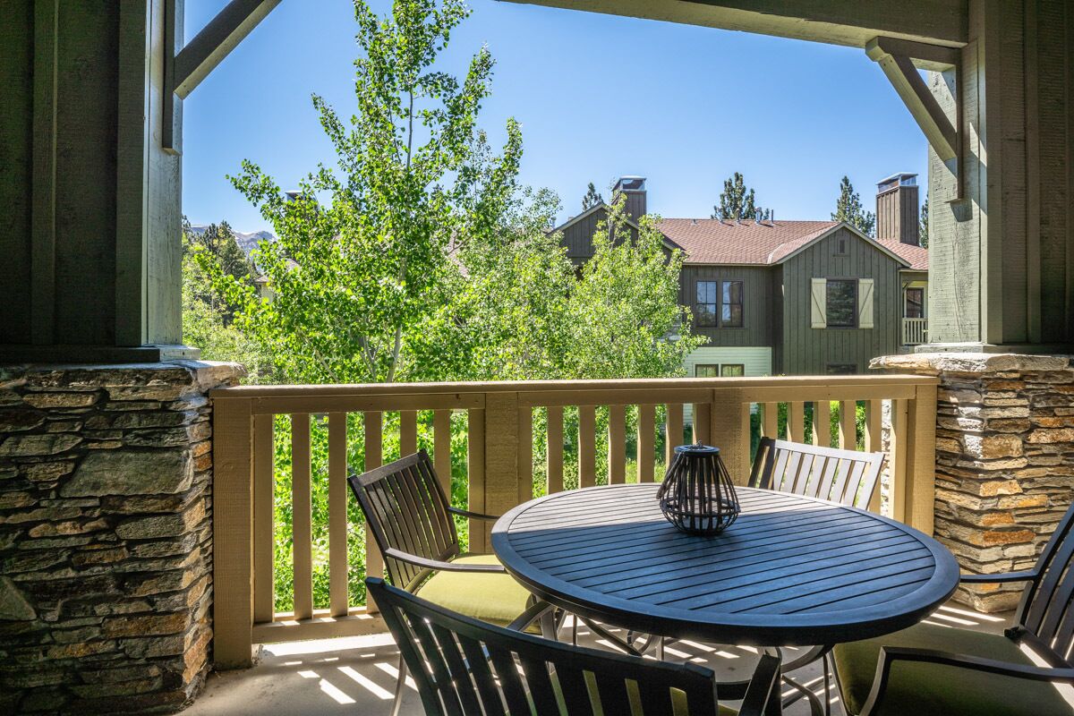 A balcony with a round table and chairs, a stone wall, and a view of houses and trees.