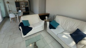 A living room with a white sofa, two armchairs, a glass coffee table, and a dining area with a glass table and chairs. - Superb air-conditioned apartment with large terrace and parking in Menton (Menton)