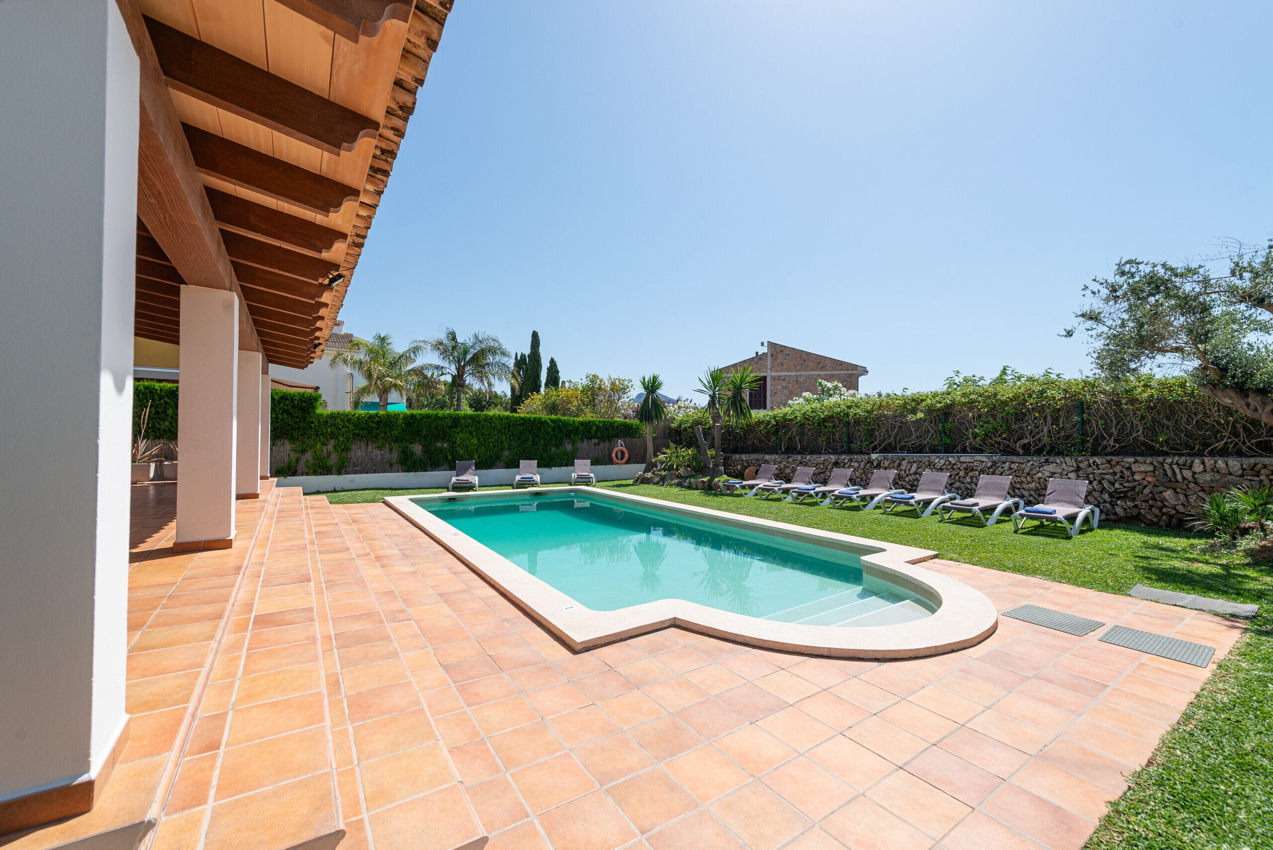 A swimming pool with a curved edge, surrounded by a tiled patio, and a covered area with wooden beams.
