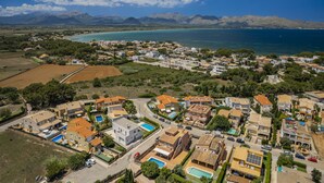 A coastal residential area with houses, a swimming pool, and a view of the sea and mountains in the background. - Large villa for 10 with private pool and beach location, near Alcudia, Mallorca (Alcudia)