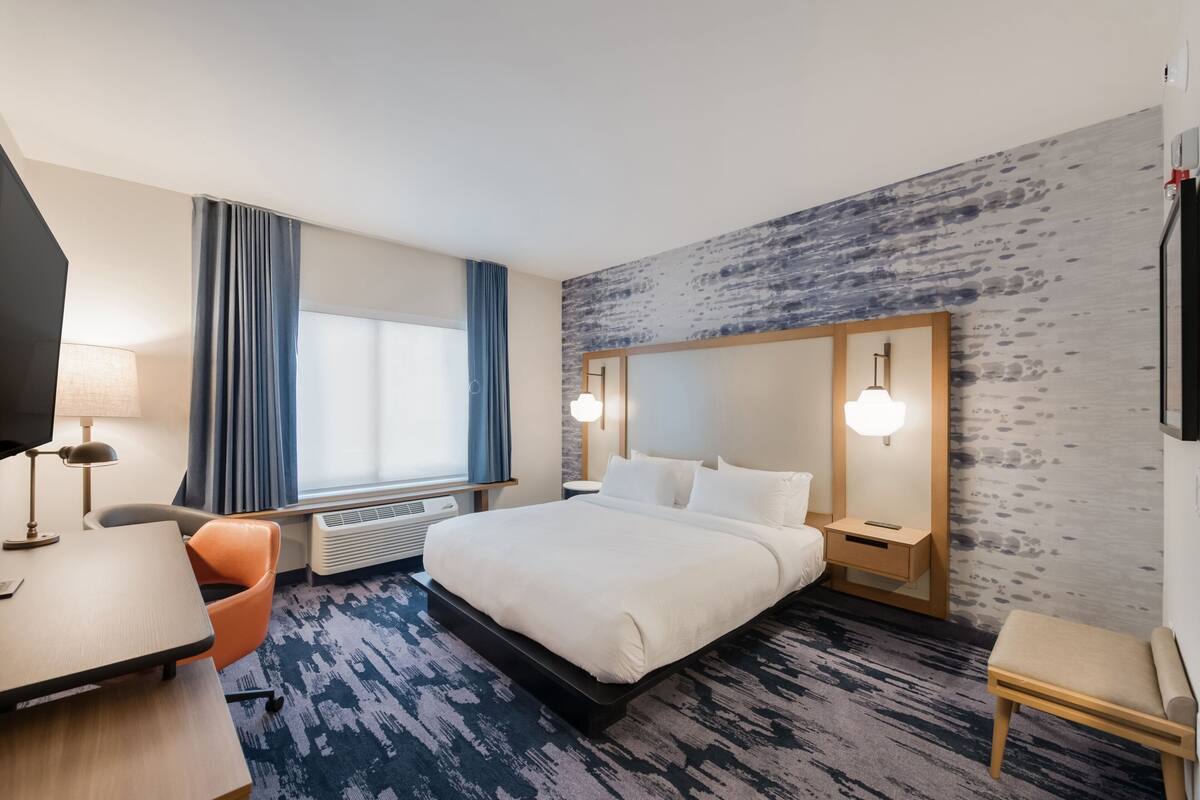 Une chambre d’hôtel avec un grand lit, un bureau, une chaise, une télévision et une fenêtre avec des rideaux.