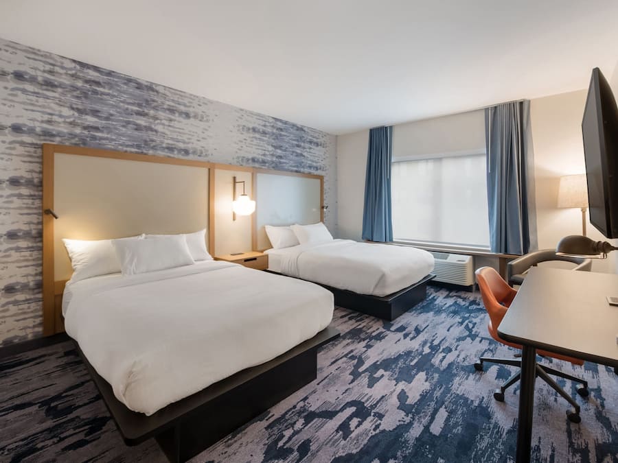 A hotel room with two beds, a desk, a chair, a TV, and a large window with curtains.