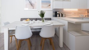 Una cocina moderna con armarios blancos, encimera de madera y comedor con dos sillas blancas y una mesa preparada para dos personas. Hay dos cuadros en la pared sobre la mesa del comedor.