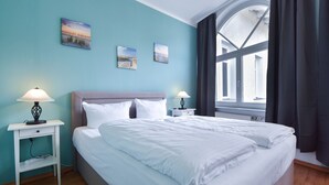 A bedroom with a large bed, two bedside tables with lamps, and a window with curtains. - Villa zur See 10 - modern maritime vacation apartment (Heringsdorf (Seebad))