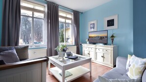 A living room with a white coffee table, grey sofa, and a TV on a white cabinet. - Villa zur See 10 - modern maritime vacation apartment (Heringsdorf (Seebad))