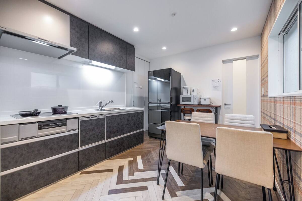 A modern kitchen with dark cabinets, a central island, and a dining area with a herringbone-patterned floor.