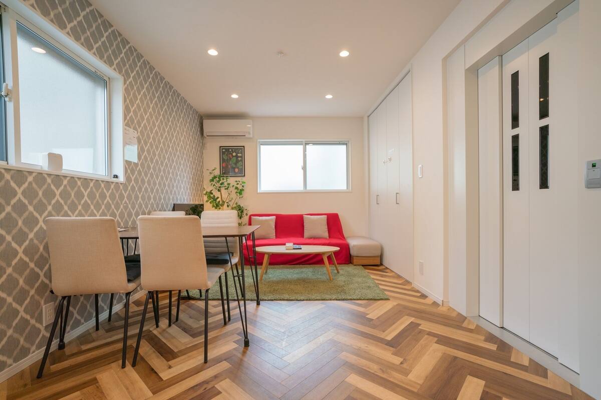 A modern living room with a red sofa, a dining table with chairs, and a herringbone-patterned floor.