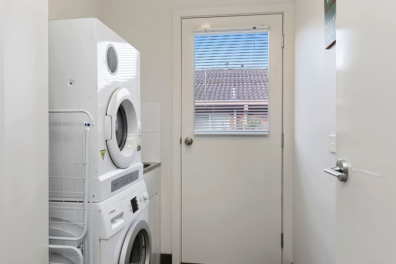 A laundry room with stacked washers and dryers, a door with a window, and a metal handle.