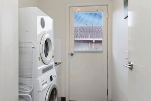Ein Waschraum mit übereinander gestapelten Waschmaschinen und Trocknern, einer Tür mit Fenster und einem Metallgriff.