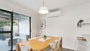 A modern dining area with a wooden table, white chairs, and a hanging pendant light.