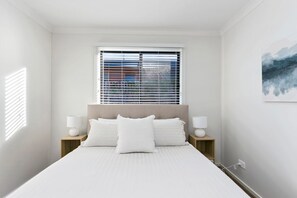 Ein Schlafzimmer mit einem Bett, zwei Nachttischen, einem Fenster mit Rollläden und einem Wandbild.