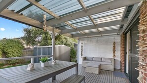 A covered outdoor area with a wooden deck, a seating area with cushions, and a wall with hanging decorations.
