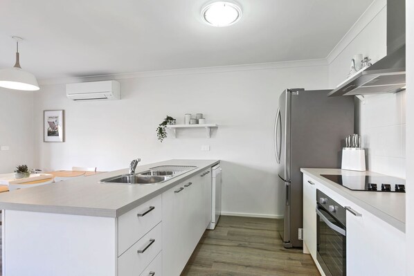A modern kitchen with white cabinetry, a stainless steel refrigerator, and a built-in oven.