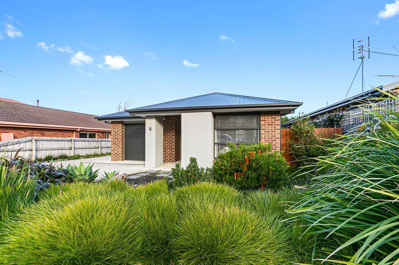 A residential house with a brick facade, a garage door, and a well-maintained garden with various plants.