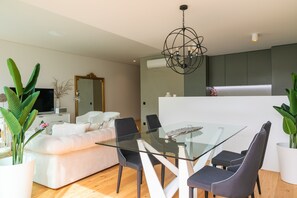 A modern living room with a glass dining table, dark chairs, a white sofa, and a large mirror.