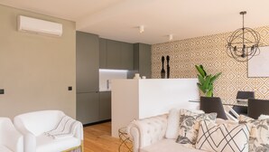 A modern living room with a white sofa, a beige sofa, and a dining area with a patterned wall and chandelier. - Ana Sofia Graça Carneiro (Porto)