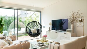 A modern living room with a large TV, comfortable seating, and a hanging chair. - Ana Sofia Graça Carneiro (Porto)