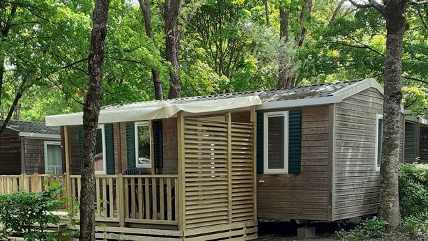 A row of wooden mobile homes with a dirt ground, surrounded by trees.