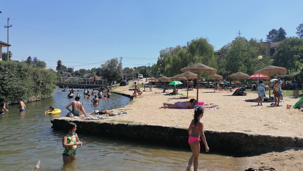 Ein Strand mit badenden und sonnenden Menschen, ein kleines Schwimmbecken und Sonnenschirme.