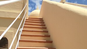 Un escalier beige, agrémenté de rampes blanches, mène à une structure surmontée d’un dôme blanc, le tout sous un ciel dégagé.