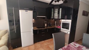 Une cuisine de taille réduite, équipée d’un réfrigérateur, d’un four et de meubles de rangement aux couleurs sombres.