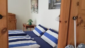 Ein Schlafzimmer mit einem hölzernen Bett, gestreifter Bettwäsche, einem kleinen Nachttisch mit Lampe und einem Bild an der Wand.
