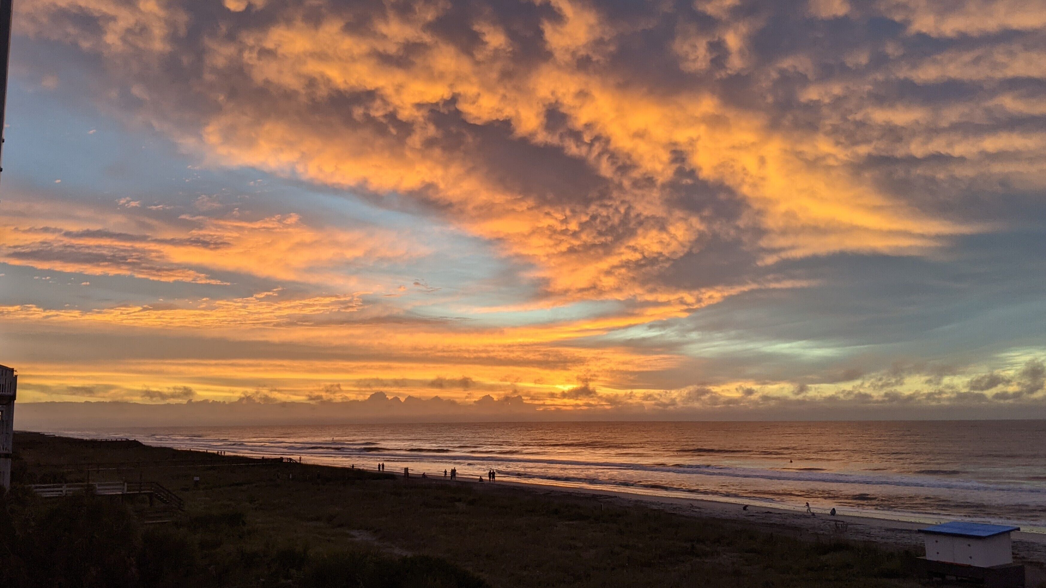 A coastal sunset with a view of the ocean and a grassy area with a fence.