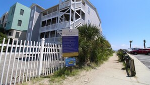 A beach house with a white fence, a signboard, and a palm tree. - Spacious Oceanfront and Pier Views~ Seaside Villas 202 (Folly Beach)