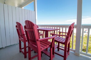 Un juego de sillón Adirondack rojo y mesa en un porche cubierto, con vista a la playa.