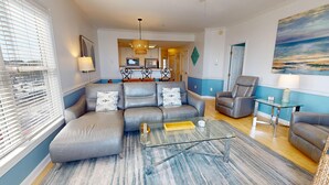 A modern living room with a sectional sofa, a glass coffee table, and a reclining chair. - Spacious Oceanfront and Pier Views~ Seaside Villas 202 (Folly Beach)