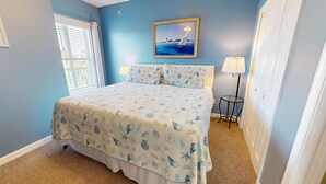 A bedroom with a bed, a nightstand, a lamp, and a painting on the wall. - Spacious Oceanfront and Pier Views~ Seaside Villas 202 (Folly Beach)