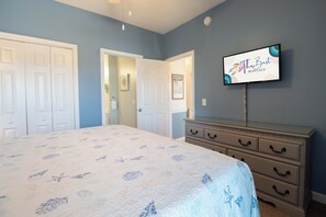A bedroom with a bed, a dresser, a television, and a door leading to another room. - Spacious Oceanfront and Pier Views~ Seaside Villas 202 (Folly Beach)