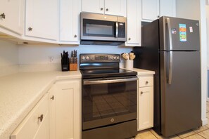 Una cocina con armarios blancos, estufa negra, microondas y refrigerador.