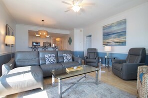 A modern living room with a sofa, chairs, a glass coffee table, and a painting on the wall. - Spacious Oceanfront and Pier Views~ Seaside Villas 202 (Folly Beach)