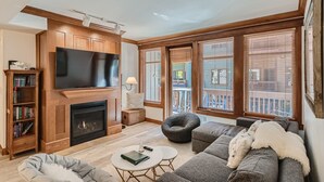 A living room with a fireplace, television, and large windows overlooking a balcony. - Mill Club 2 Bedroom Condo!!  Ski In/Out in Copper's Center Village!! (Copper Mountain)