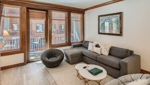 A modern living room with a sectional sofa, a round coffee table, a bean bag chair, and a large window with blinds. - Mill Club 2 Bedroom Condo!!  Ski In/Out in Copper's Center Village!! (Copper Mountain)