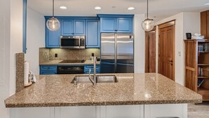 A modern kitchen with blue cabinets, stainless steel appliances, granite countertops, and pendant lighting. - Mill Club 2 Bedroom Condo!!  Ski In/Out in Copper's Center Village!! (Copper Mountain)