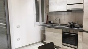 A modern kitchen with white cabinets, a stainless steel sink, and an oven. There is a dining table with chairs and a decorative centerpiece. - Case Vacanza "Le Cale - Cala Goloritzè" (Tortolì)