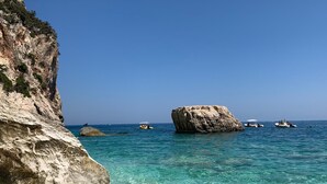 A coastal scene with clear turquoise waters, rocky cliffs, and several boats. - Case Vacanza "Le Cale - Cala Goloritzè" (Tortolì)