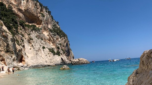 A coastal scene with clear turquoise waters, rocky cliffs, and boats in the distance. - Case Vacanza "Le Cale - Cala Goloritzè" (Tortolì)